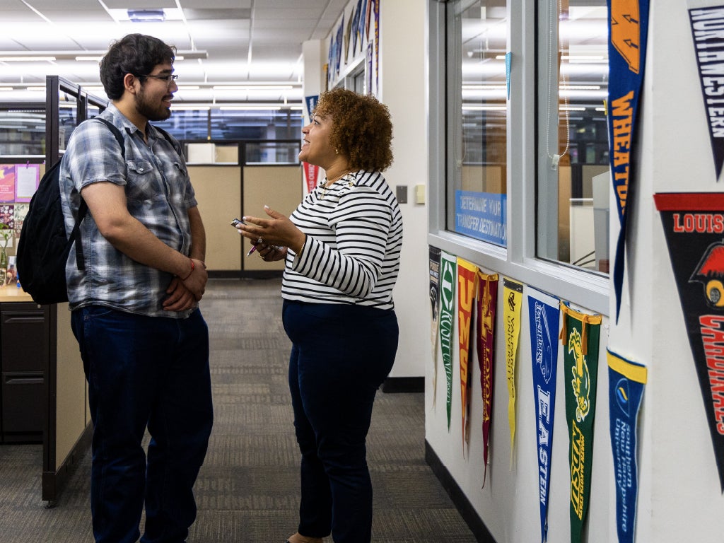 Transfer Events Advisor talking with a student in an office decorated with college pennants